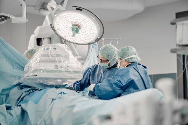 Zwei Ärzte stehen unter einer großen OP Leuchte in einem modernen Hybrid OP.