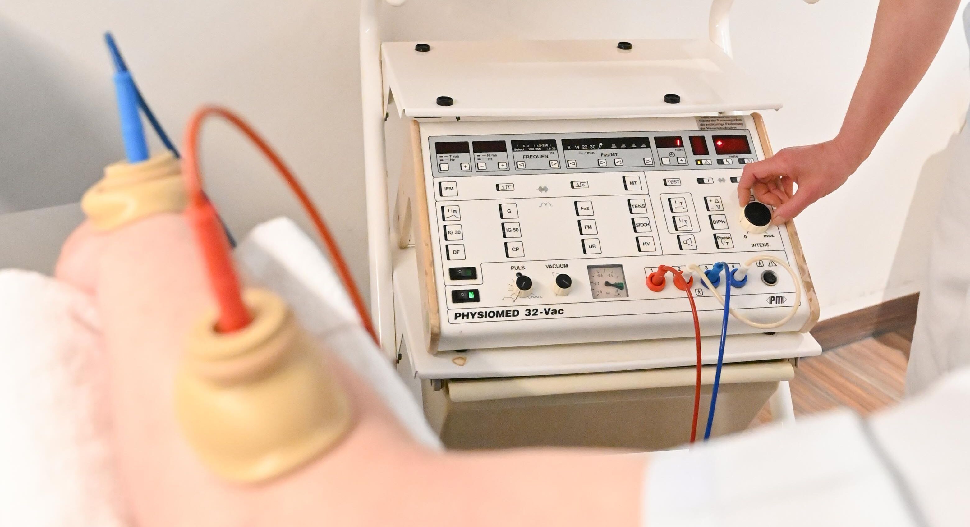 Ärztin behandelt Patienten mit Elektrotheraie über zwei angesteckten Stöpsel am Arm und einer Apparatur mit einigen Knöpfen .