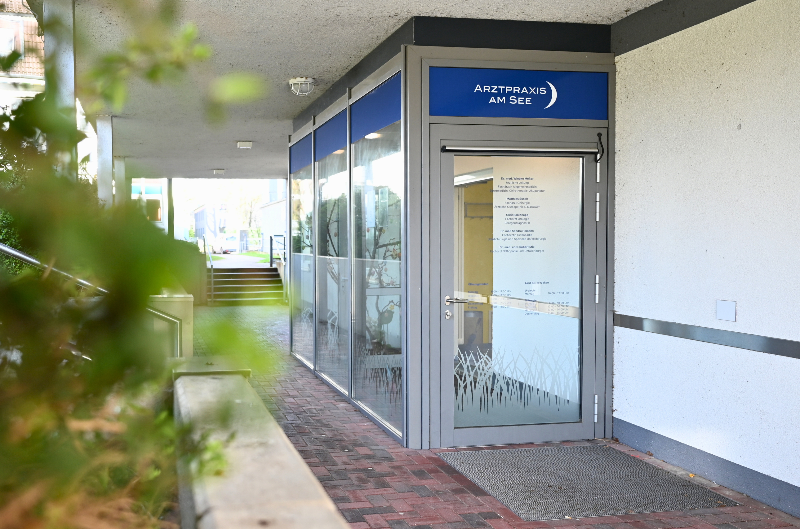 Glastür zur Praxis am See liegt in einem sonnigen Gang an der Seite des Gebäudes der Allgemeinen Klinik.
