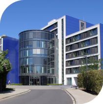 Am Ende einer ruhigen Straße liegt große, gläserne, moderne Klinik direkt vor dem Segeberger See. Neben der Klinik stehen einige Bäume und Sträucher.