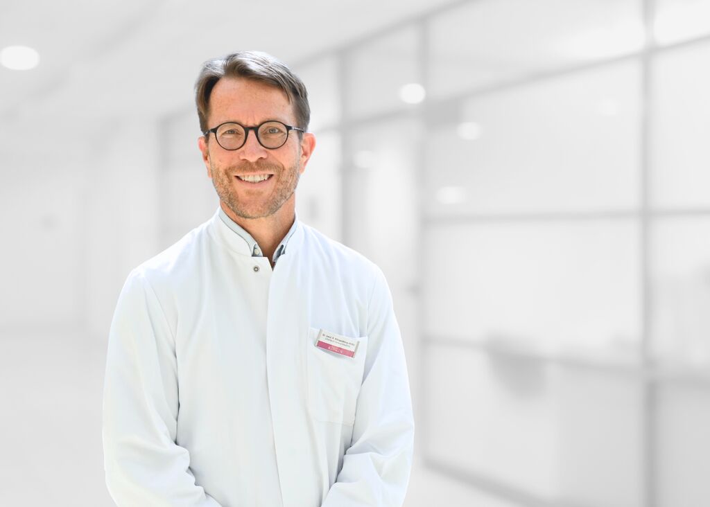 Blonder Mann mittleren Alters im weißen Arztkittel und Brille