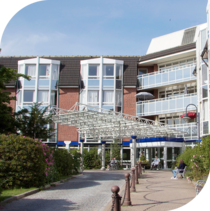 Breite Einfahrt führt zu roten Backstein Haus mit vielen Balkonen und großen Fenstern.