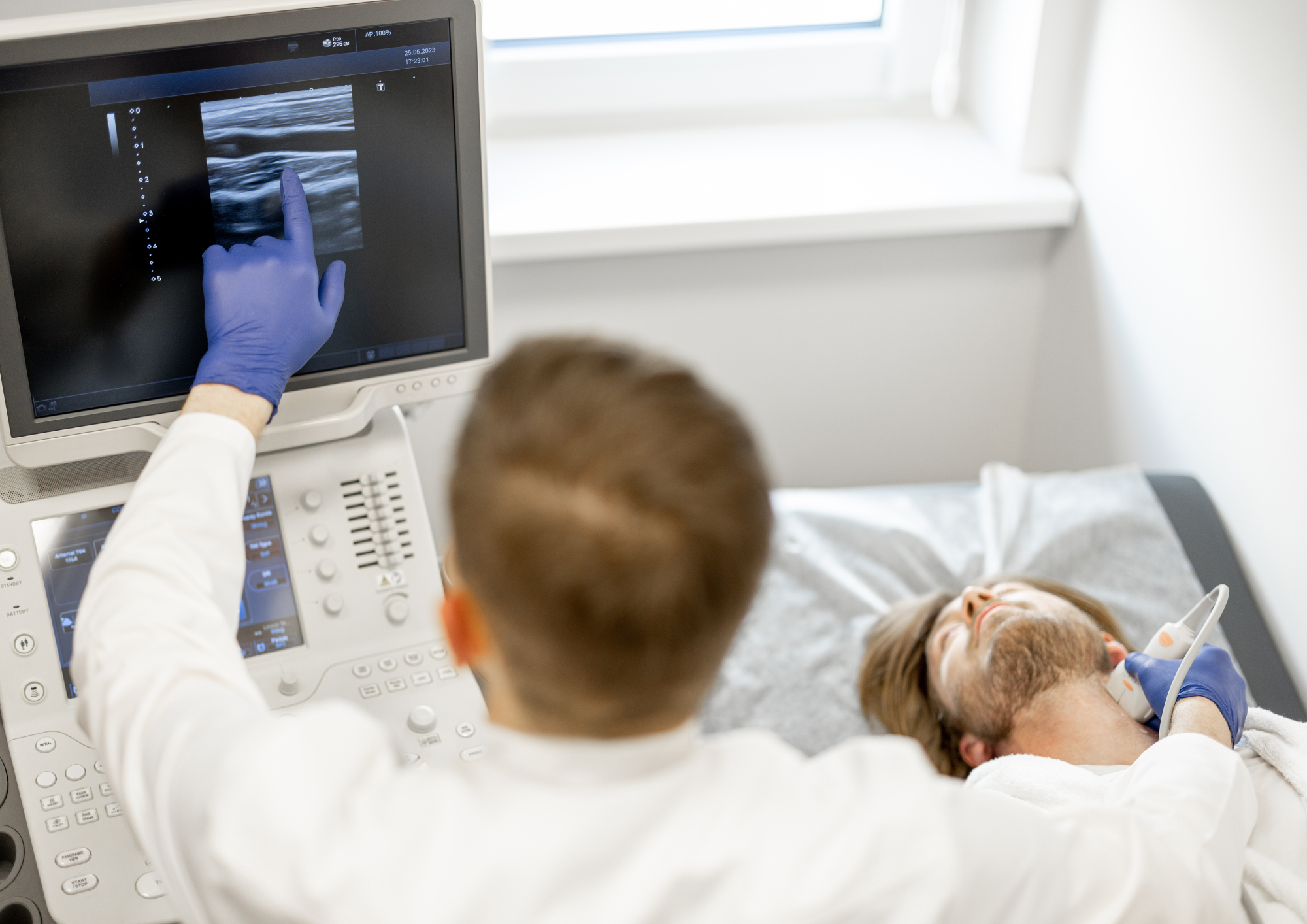 Ein Arzt untersucht einen Mann an der Halsschlagader mit einem Ultraschallgerät.