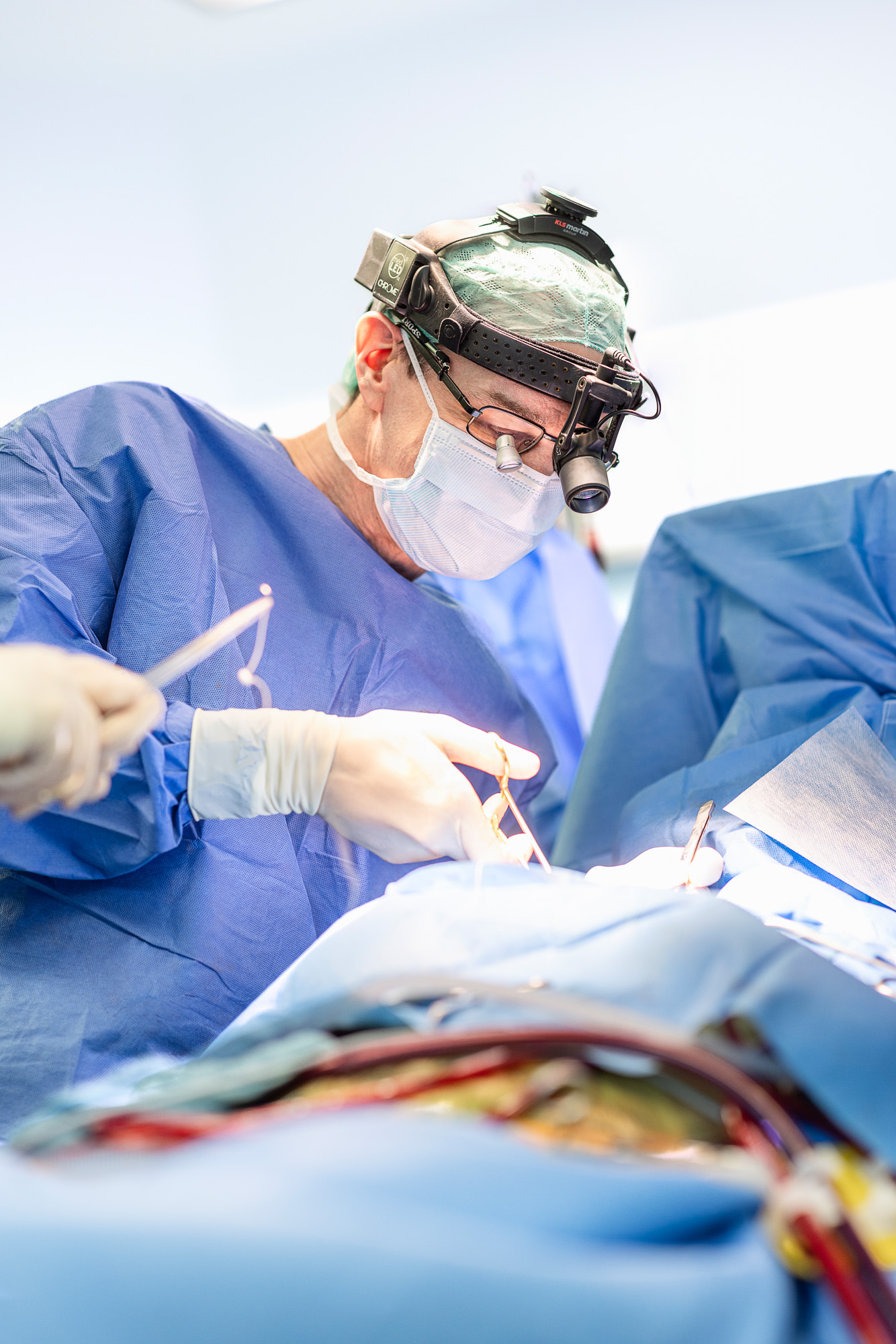 Operateur steht mit Lampe an der Stirn am Op Tisch.